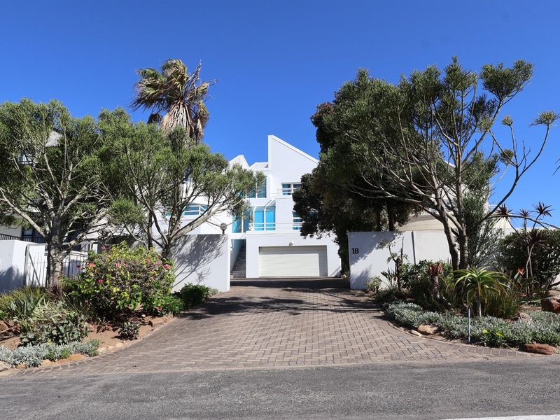 A modern multi-level residential property featuring a paved driveway, secure garage, and landscaped front garden with established trees.