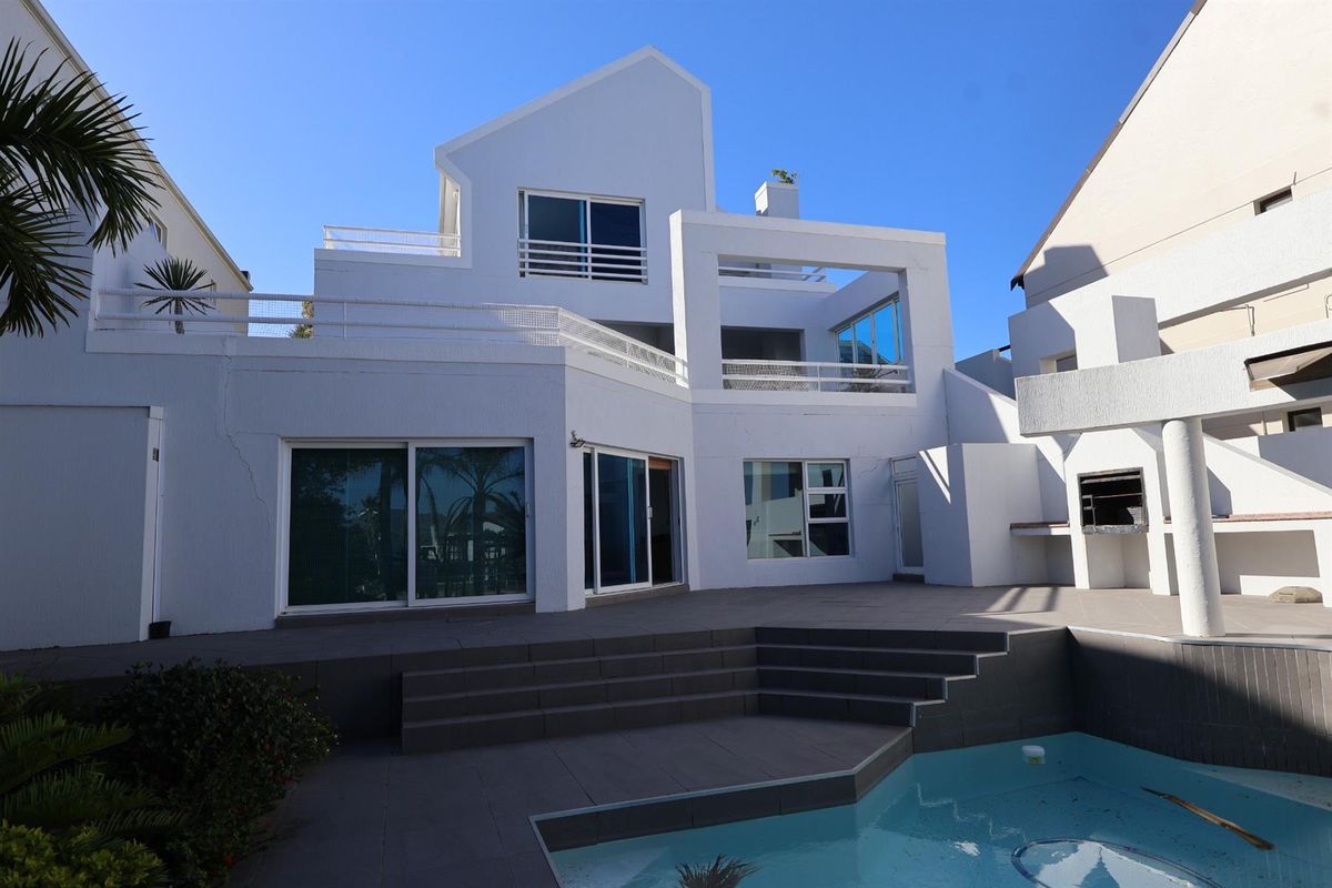 Rear exterior view of a multi-level home featuring a swimming pool, tiled patio area, built-in braai, and balcony access.