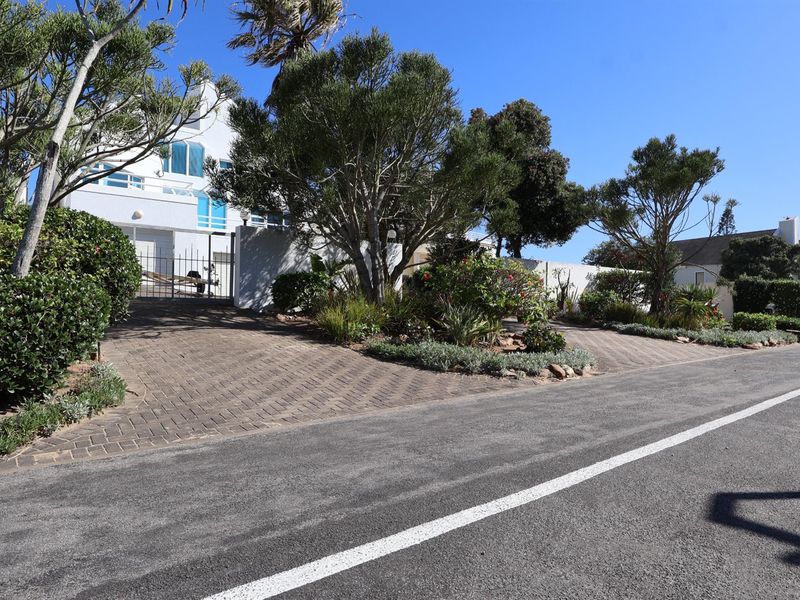 A view of the property entrance from the street, featuring a paved driveway, landscaped garden, and white building facade.