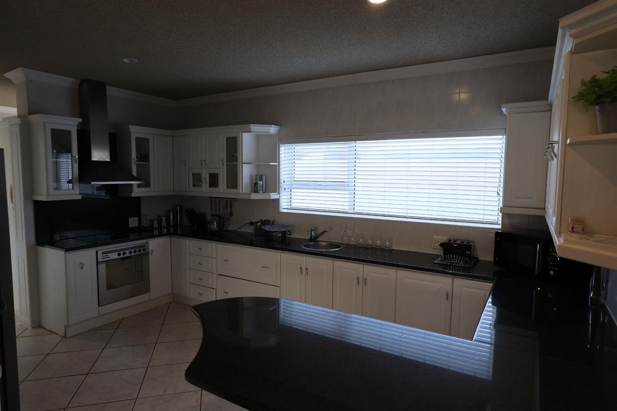 A functional kitchen featuring white cabinetry, dark granite countertops, a built-in oven, stainless steel extractor fan, and tiled flooring.