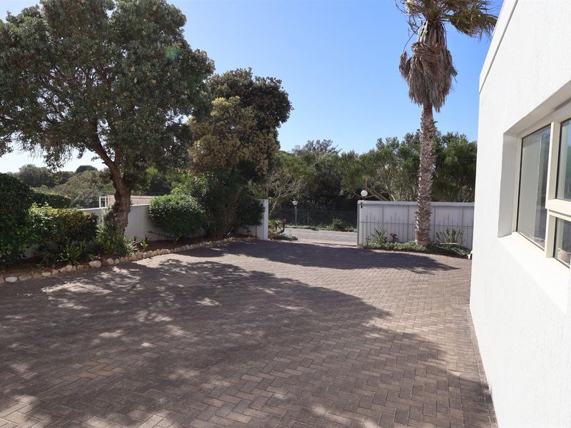 A paved driveway area leading to the property entrance, featuring established trees, landscaped garden borders, and a white boundary wall.