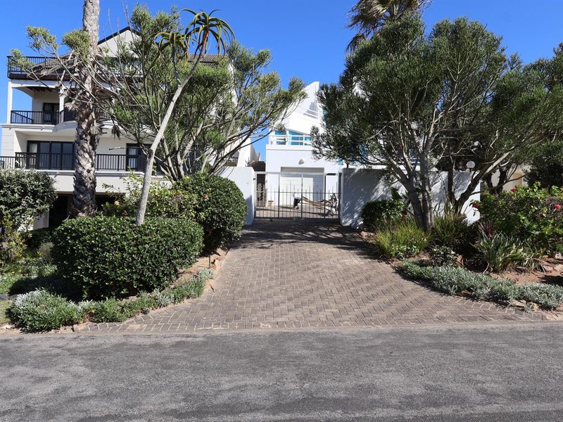 A paved driveway leading to a secure gated entrance with mature landscaping and a multi-story residential building in the background.