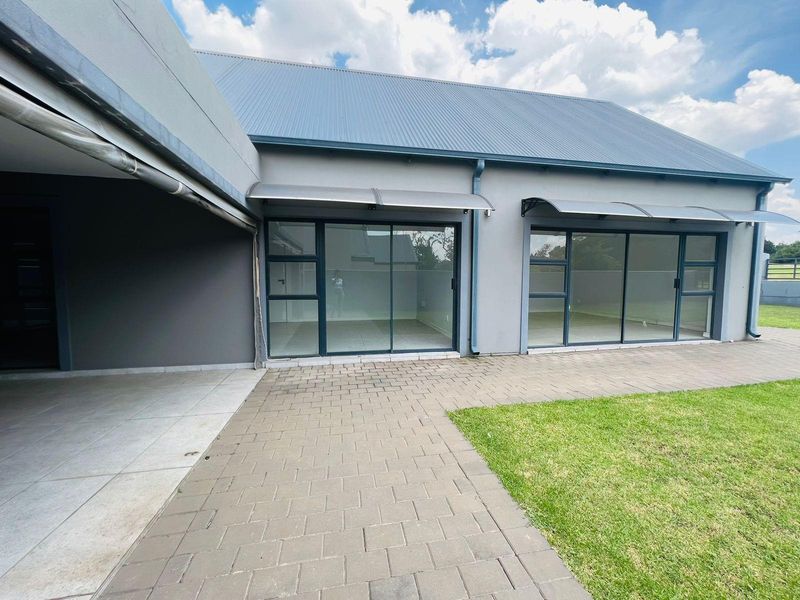 Rear exterior view featuring a paved patio area, large sliding glass doors, and modern metal awnings leading into the home.