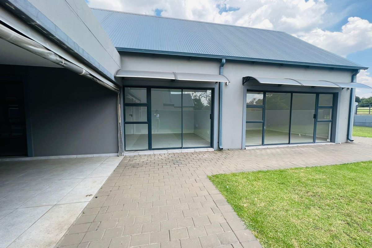 Rear exterior view featuring a paved patio area, large sliding glass doors, and modern metal awnings leading into the home.