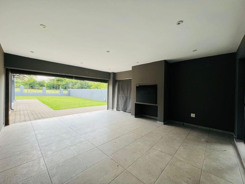 A spacious covered patio featuring tiled flooring, recessed ceiling lighting, and a built-in fireplace, opening directly onto a private rear garden.