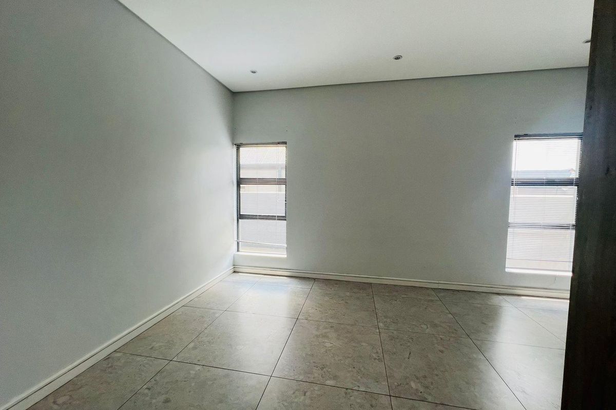 A bright, empty bedroom featuring neutral tiled flooring, recessed ceiling lighting, and two windows fitted with horizontal blinds.