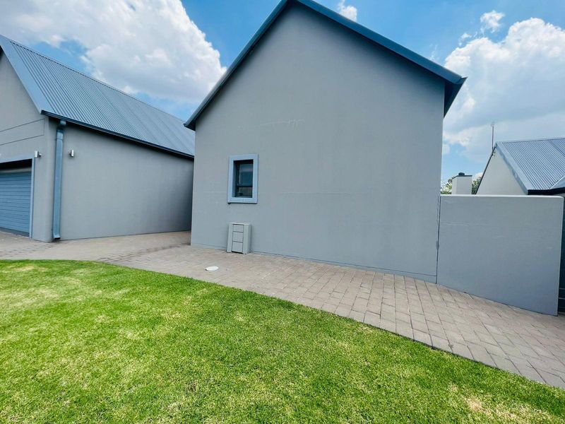 A view of the rear exterior of the house featuring paved walkways, a manicured lawn, and modern grey painted walls with metal roofing.