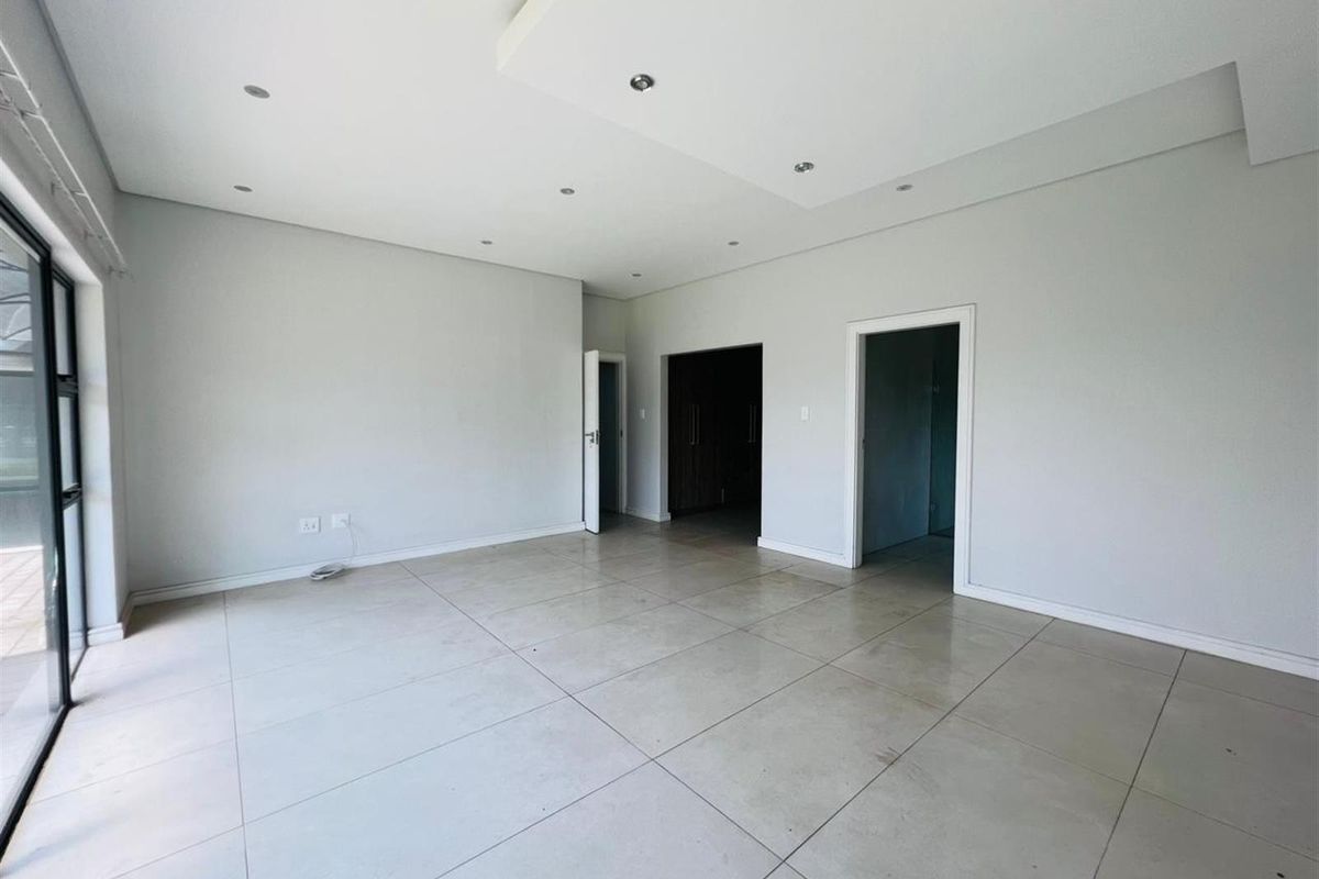 A spacious, open-plan living area featuring large format floor tiles, recessed ceiling lighting, and sliding glass doors leading to an outdoor space.