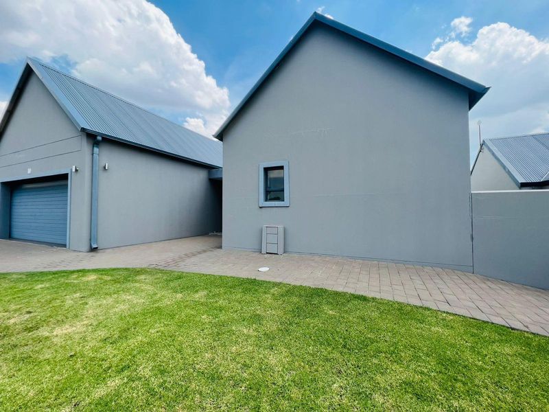 A view of the exterior rear of the property, featuring a paved walkway, manicured lawn, and modern grey facade with a garage.
