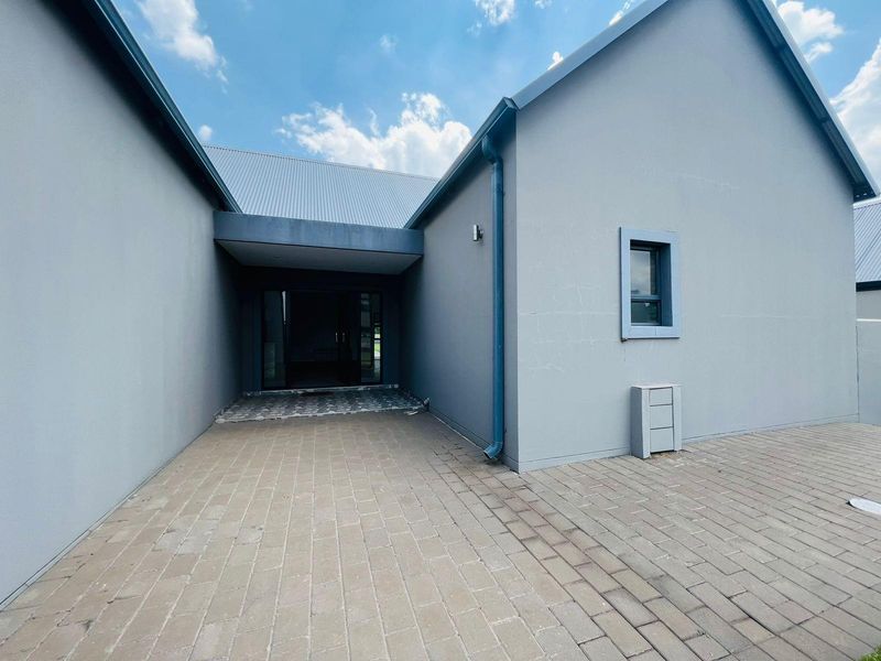 A modern exterior entrance area featuring paved flooring, a covered walkway, and clean grey rendered walls with a metal roof.
