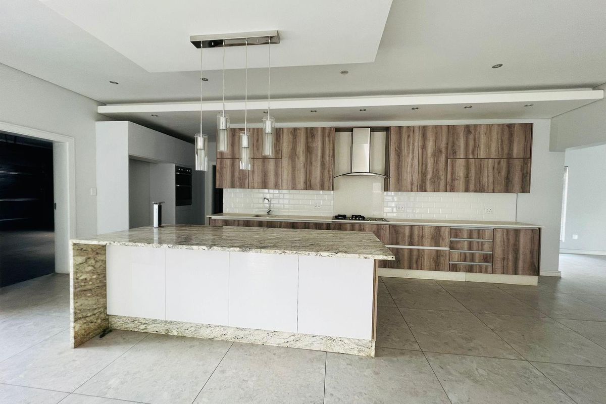 Modern open-plan kitchen featuring wood-grain cabinetry, granite countertops, a central island, built-in oven, and stainless steel extractor fan.