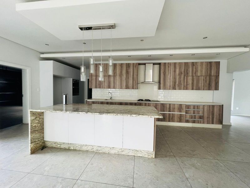 Modern open-plan kitchen featuring wood-grain cabinetry, granite countertops, a central island, built-in oven, and stainless steel extractor fan.