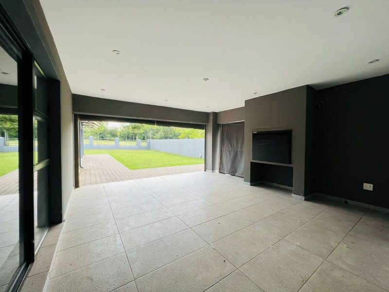Spacious covered patio featuring large format floor tiles, recessed ceiling lighting, and a built-in braai, opening directly onto a landscaped garden.