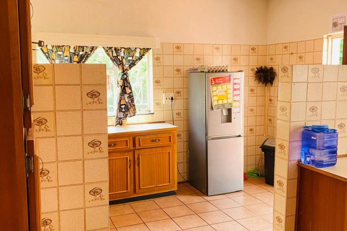 A dated kitchen featuring tiled walls, ceramic floor tiles, and built-in wooden cabinetry with a functional layout.