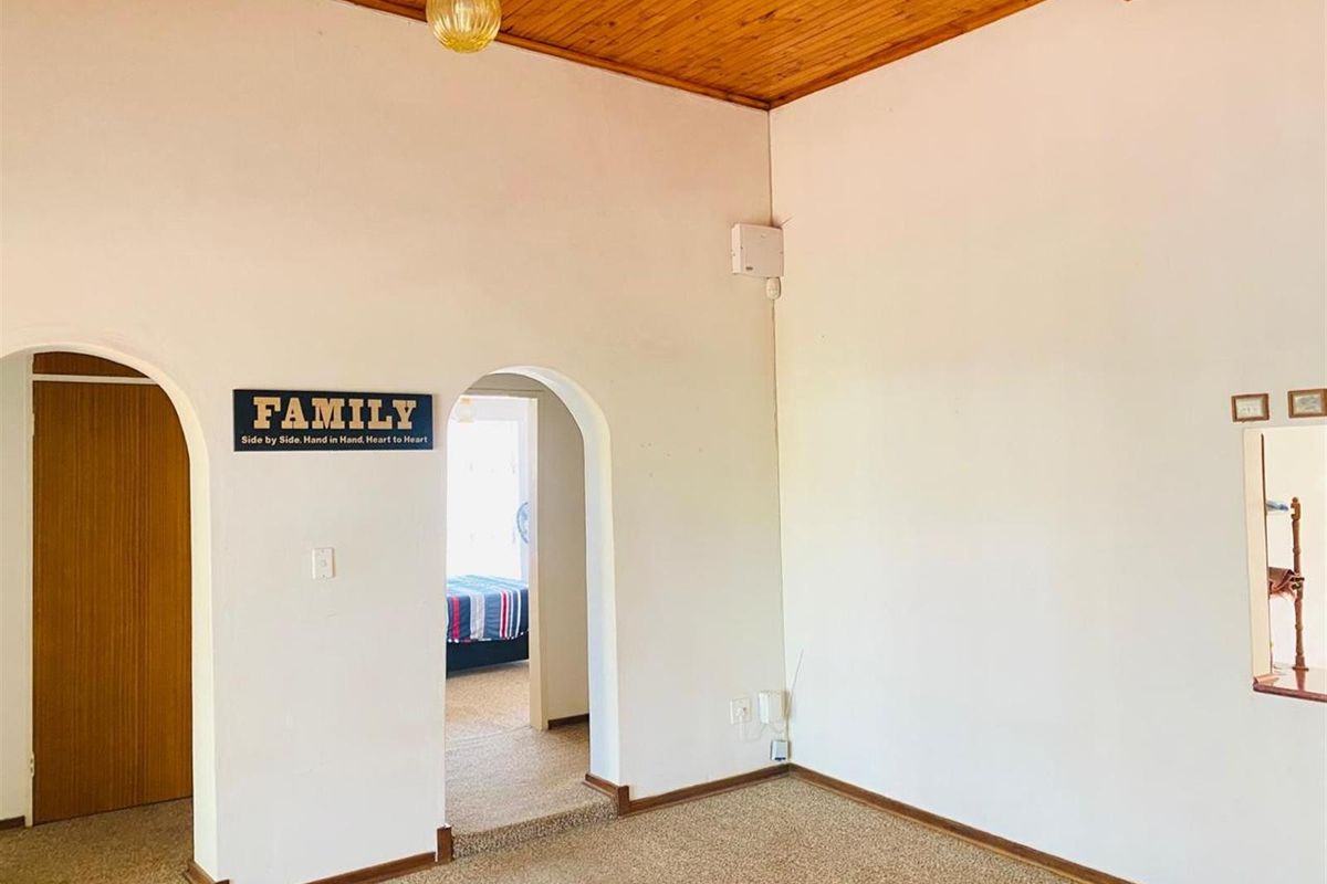 A living area featuring arched doorways, a timber-clad vaulted ceiling, and carpeted flooring, providing a neutral foundation for interior updates.