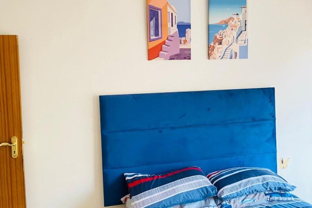 A bedroom featuring a blue upholstered headboard, neutral walls, and carpeted flooring.