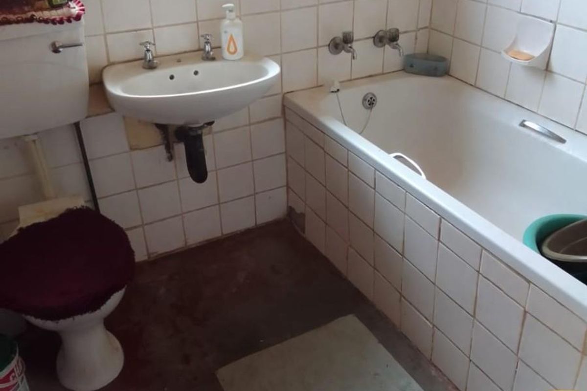 A functional bathroom featuring a standard bathtub, wall-mounted basin, and toilet with tiled splashbacks and a security-barred window.