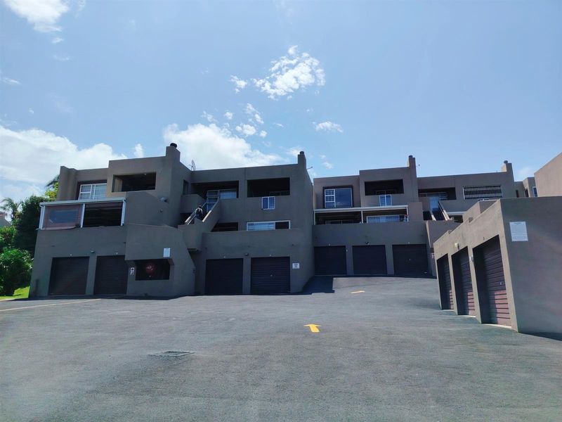 Exterior view of an apartment complex featuring multiple garage units, paved driveway access, and upper-level balconies with security fixtures.