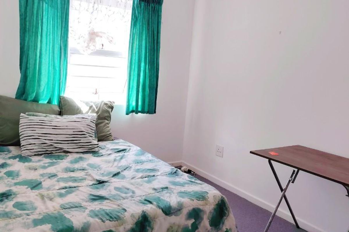 A simple bedroom featuring carpeted flooring and a window with curtains.