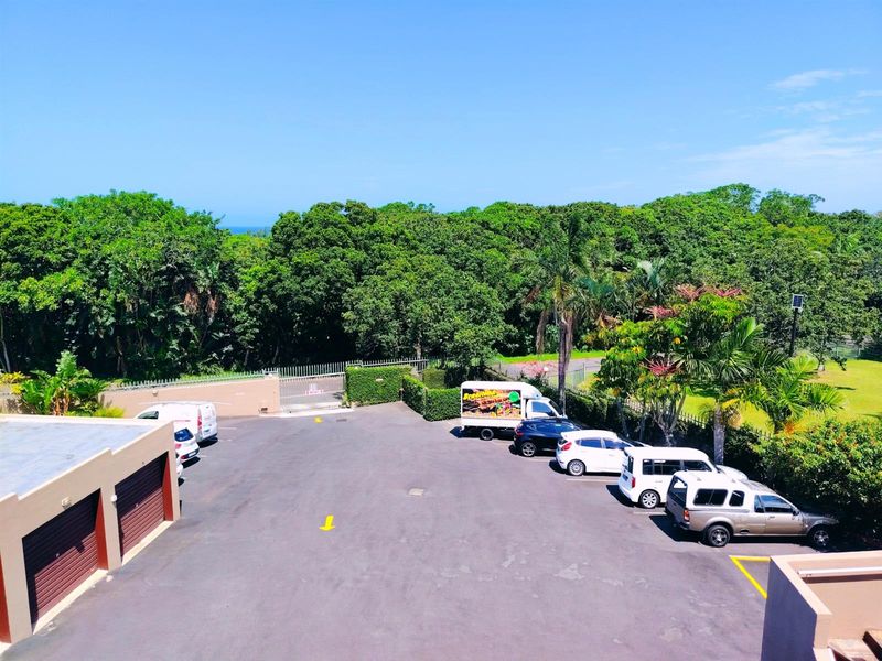 An elevated view of the property's rear exterior, featuring a paved driveway, garage access, and surrounding landscaped garden area.