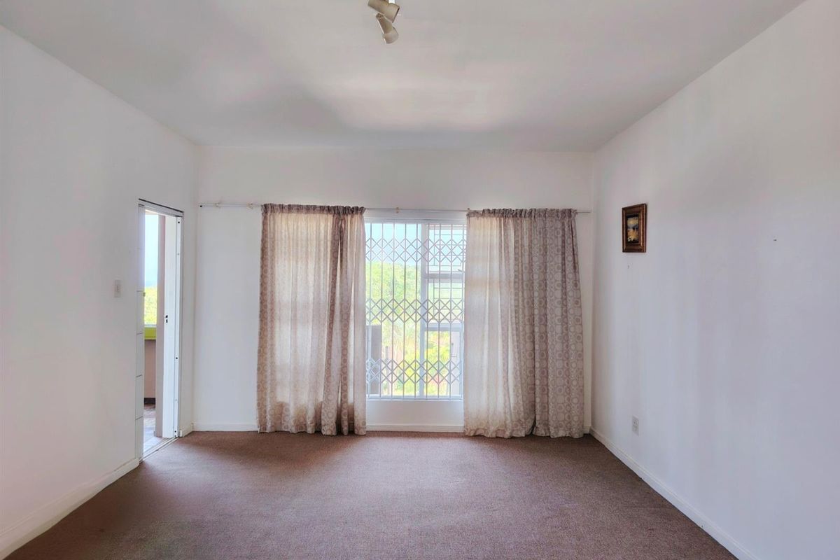 A spacious, empty living room featuring neutral walls, carpeted flooring, and a security gate on the window, offering a blank canvas for personalization.