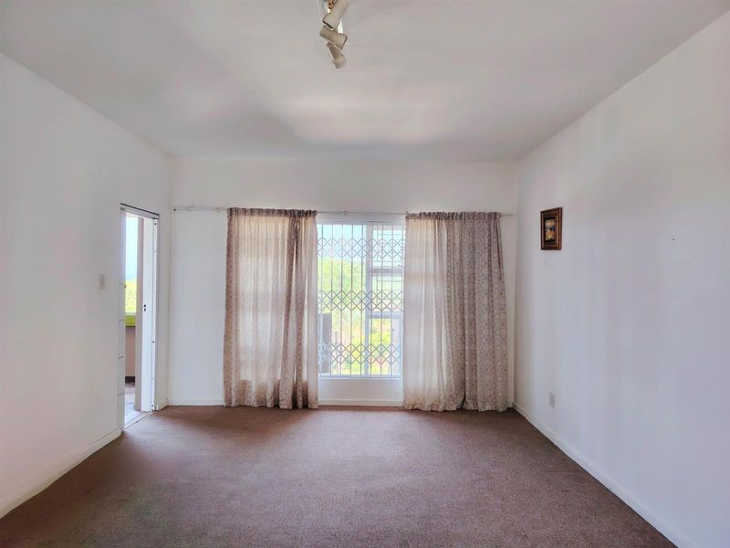 A spacious, empty living room featuring neutral walls, carpeted flooring, and a security gate on the window, offering a blank canvas for personalization.