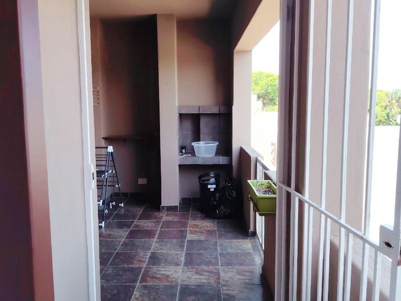 A covered balcony area featuring tiled flooring, a built-in braai, and a secure metal gate entrance.
