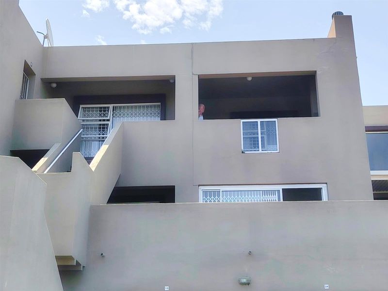 Exterior view of an apartment building featuring balconies, external staircases, and security gates on windows.