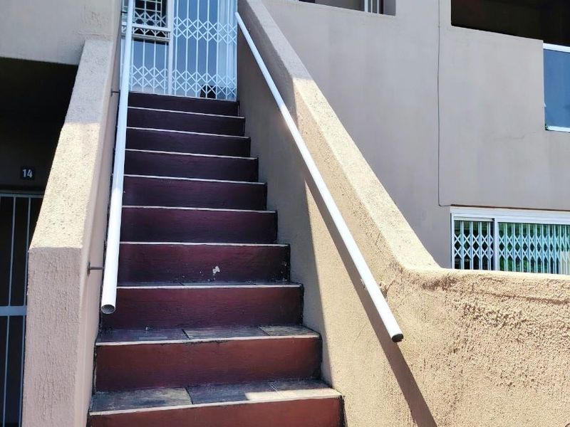 Exterior view of an apartment entrance featuring a tiled staircase with a security gate and handrail.
