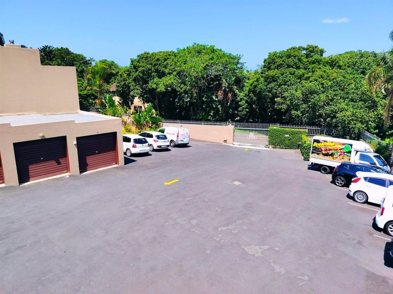 Aerial view of the apartment complex parking area featuring asphalt paving, multiple garage units, and secure perimeter fencing.