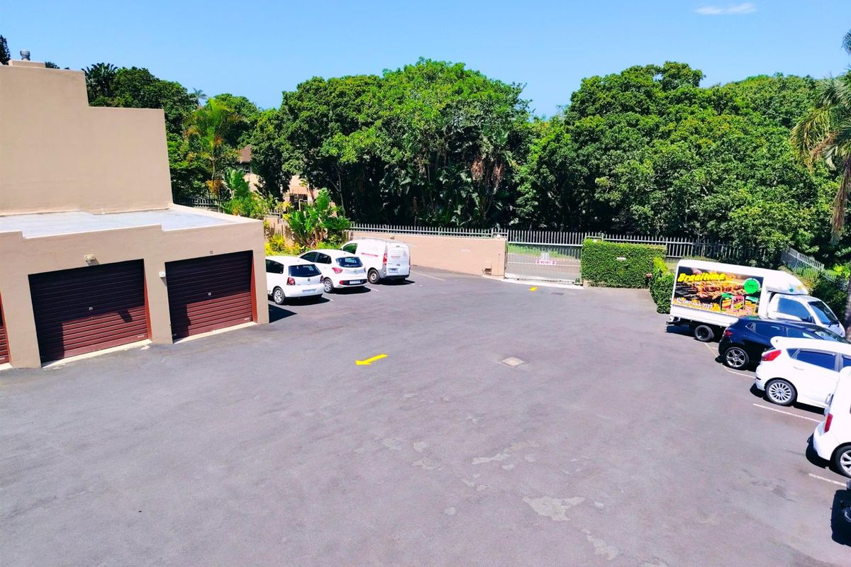 Aerial view of the apartment complex parking area featuring asphalt paving, multiple garage units, and secure perimeter fencing.