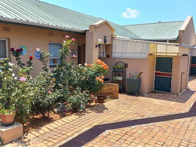 Front entrance view of a retirement village unit featuring a paved walkway, corrugated metal roofing, and a stable-style door.