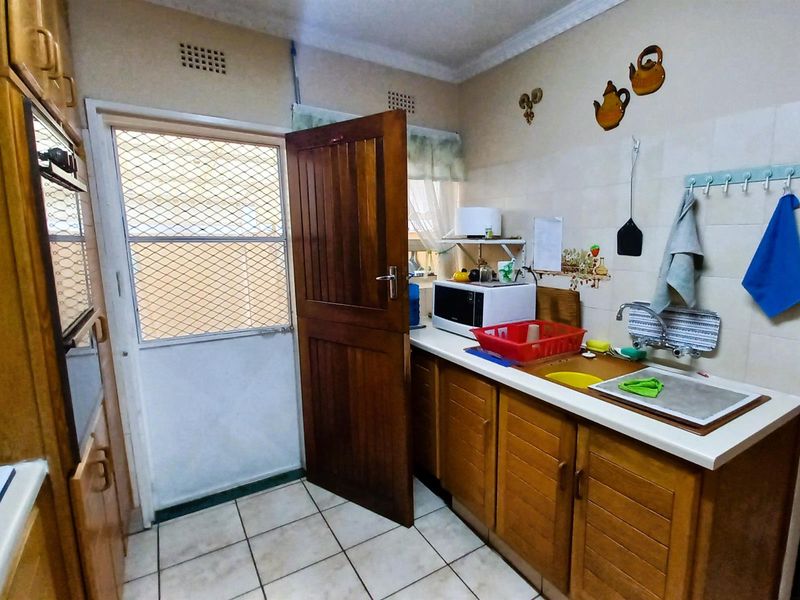 A functional kitchen featuring wooden cabinetry, tiled backsplash, built-in oven, and direct access to an exterior security door.