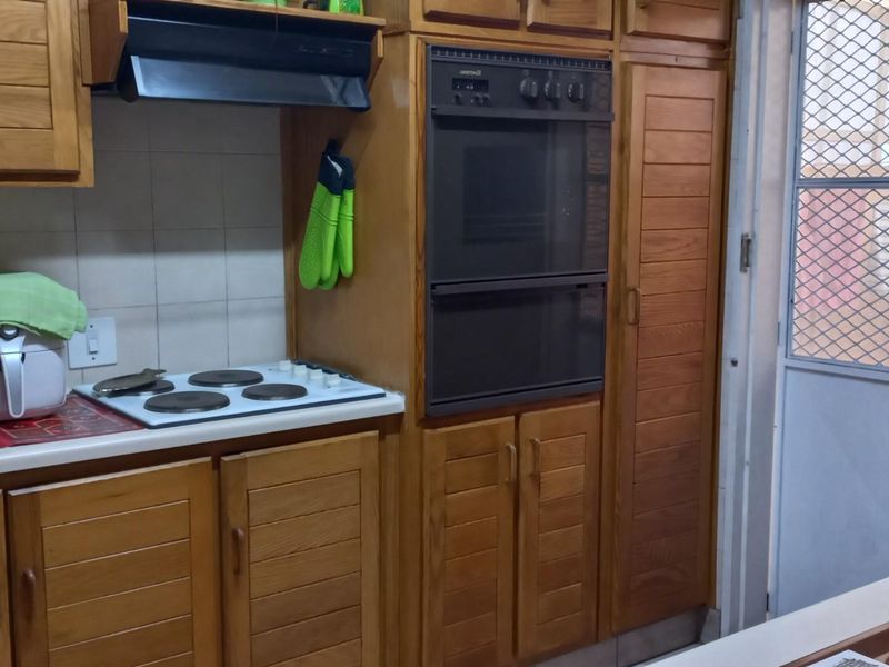 Functional kitchen featuring traditional timber cabinetry, built-in double oven, electric cooktop, and direct access to an outdoor area via a security screen door.