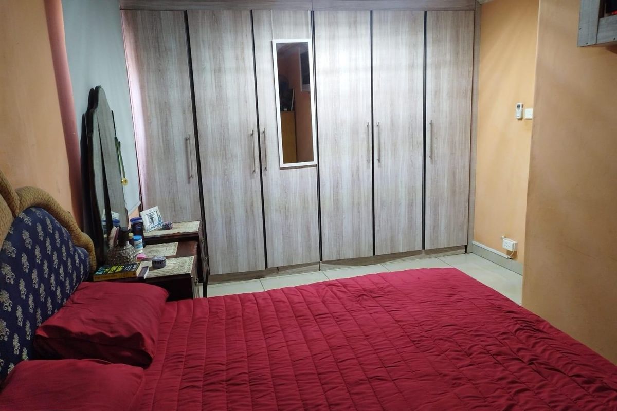 A bedroom featuring built-in floor-to-ceiling wooden wardrobes with a central mirror panel and tiled flooring.