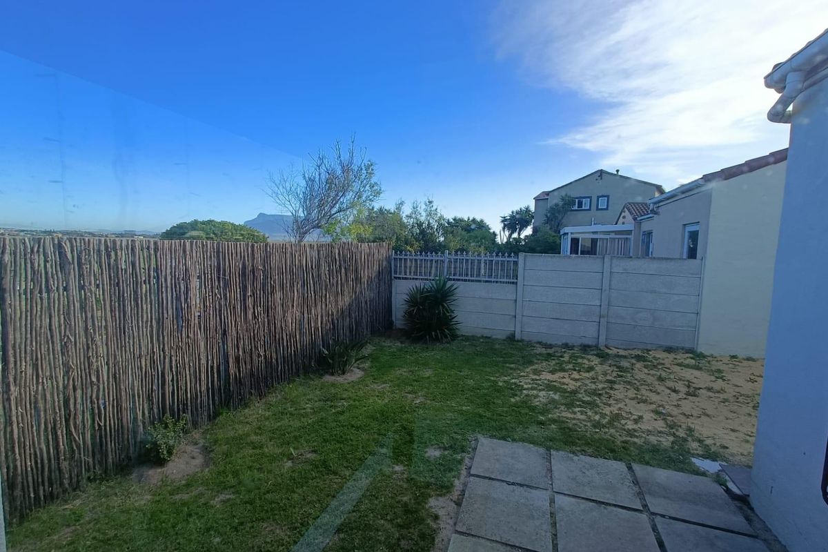 A rear garden area featuring a combination of lawn, paving slabs, and a mix of stick and precast concrete boundary fencing.