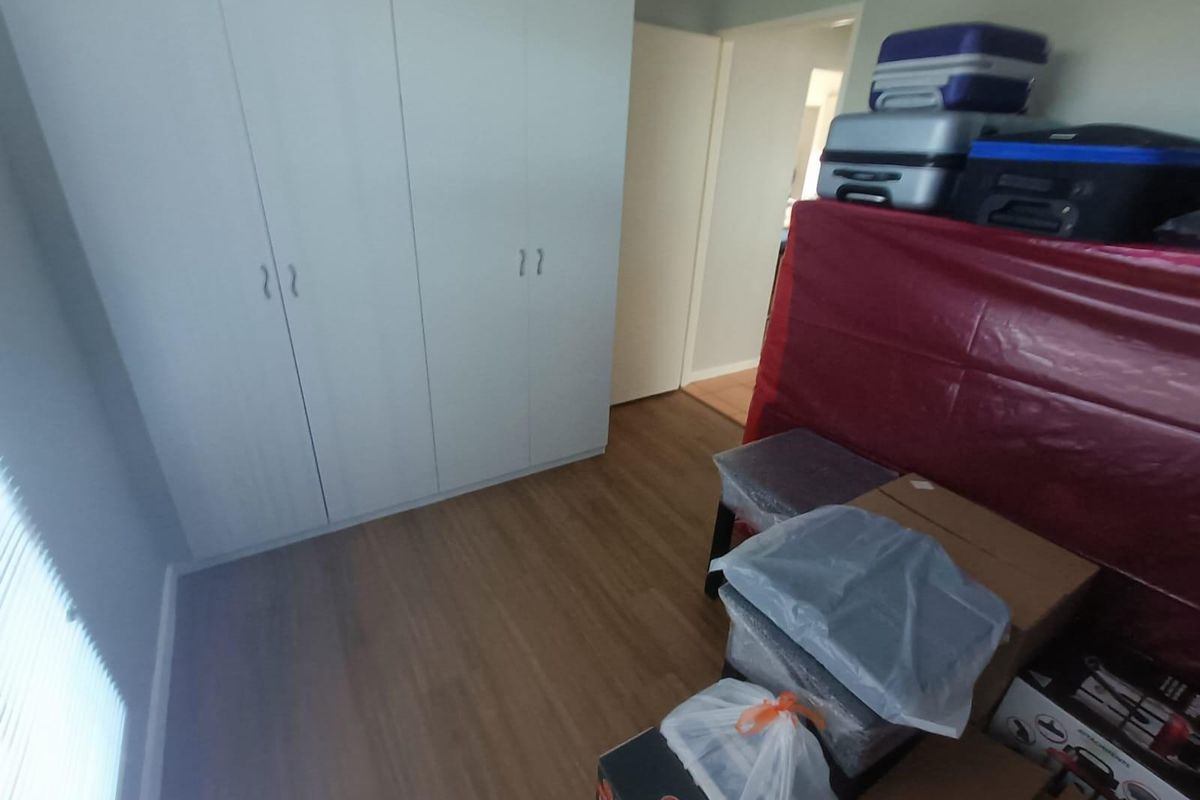 A bedroom featuring built-in cupboards and laminate flooring, currently used for storage.