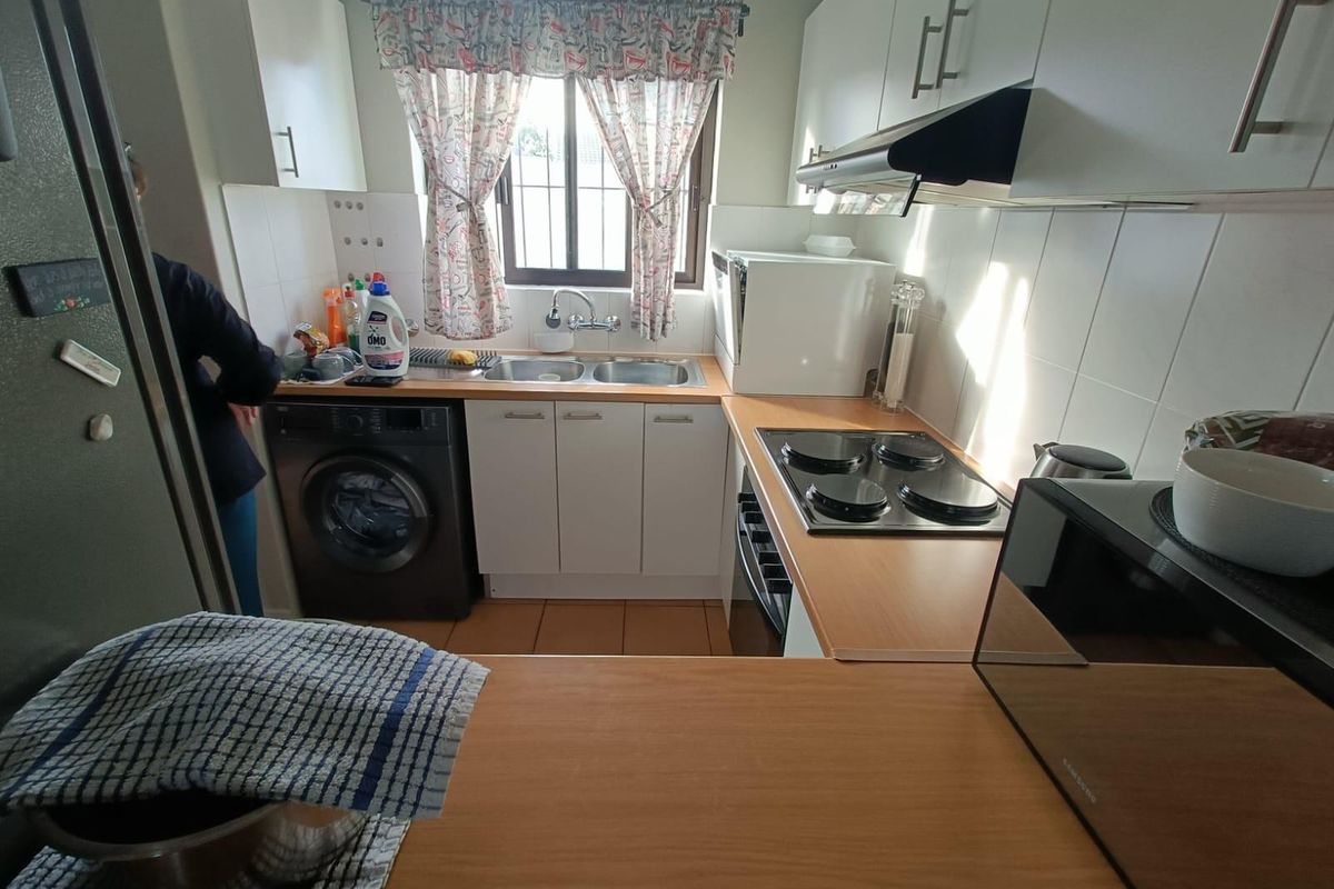 Compact kitchen featuring white cabinetry, laminate countertops, integrated electric hob, extractor fan, and a double sink with tiled backsplash.
