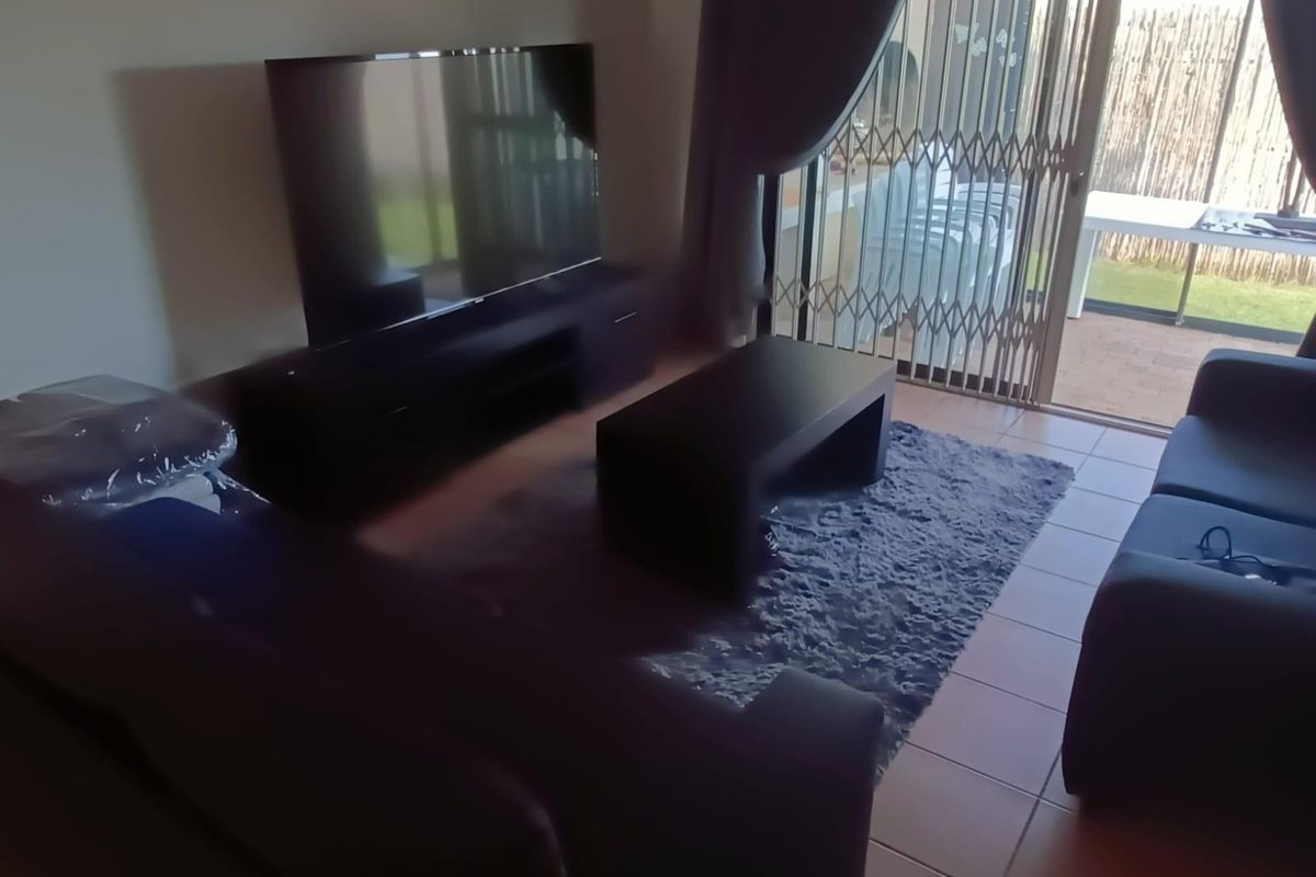 A living room featuring tiled flooring and a sliding glass door with a security gate, providing direct access to the outdoor patio area.