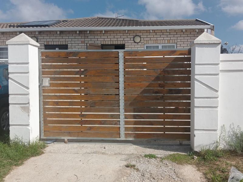 Front view of the property featuring a timber slat gate, masonry pillars, and a boundary wall with a tiled roof visible in the background.