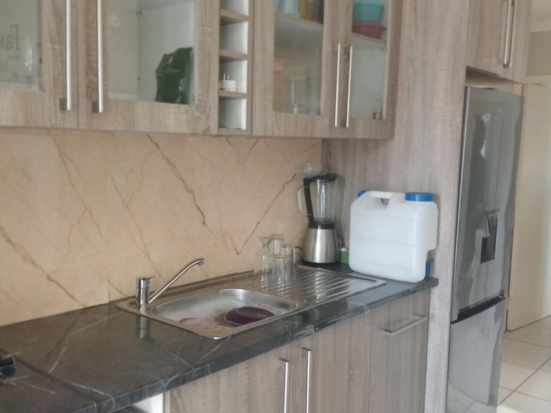 A functional kitchen featuring wood-look laminate cabinetry, stone-effect countertops, a stainless steel sink, and a decorative tiled splashback.
