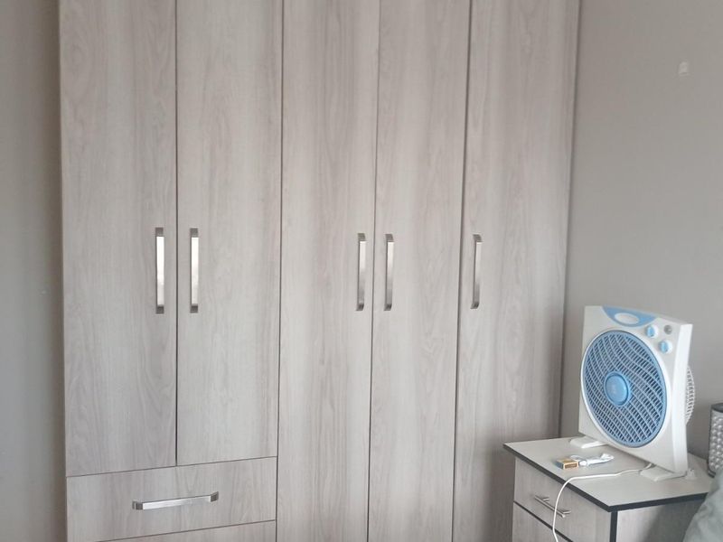 A bedroom featuring a modern, light wood-grain built-in wardrobe with integrated drawers and sleek metal handles.
