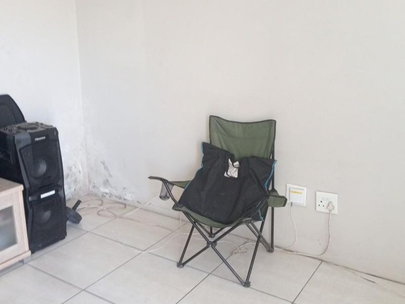 A sparsely furnished living area featuring tiled flooring and visible wall damage requiring maintenance.