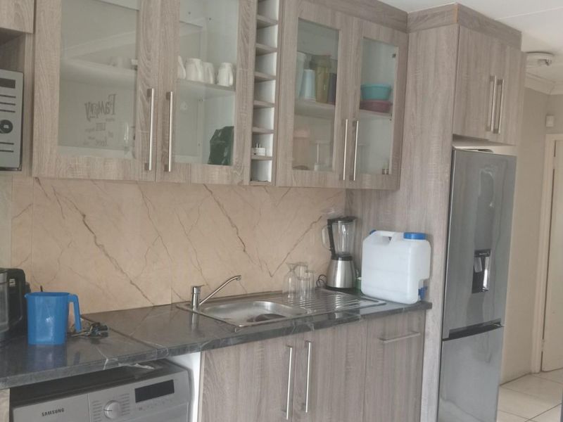 A functional kitchen area featuring wood-grain laminate cabinetry, a stone-look splashback, integrated sink, and space for a washing machine.