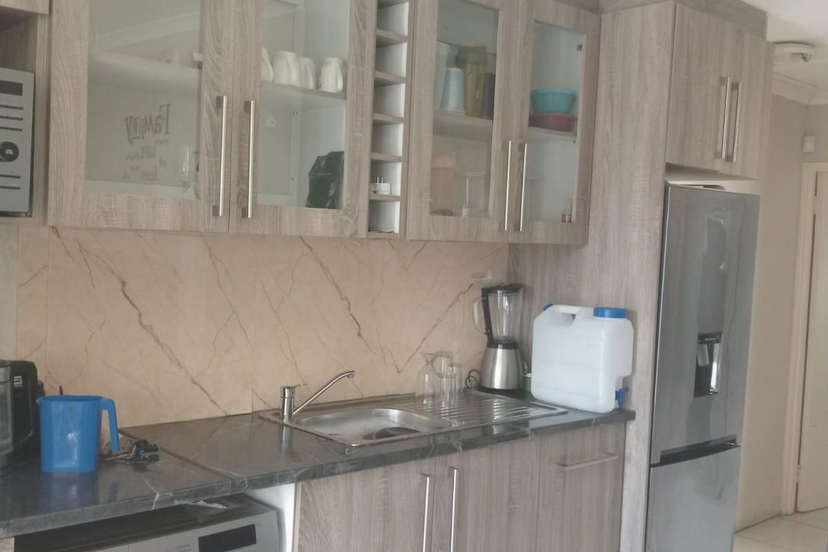 A functional kitchen area featuring wood-grain laminate cabinetry, a stone-look splashback, integrated sink, and space for a washing machine.