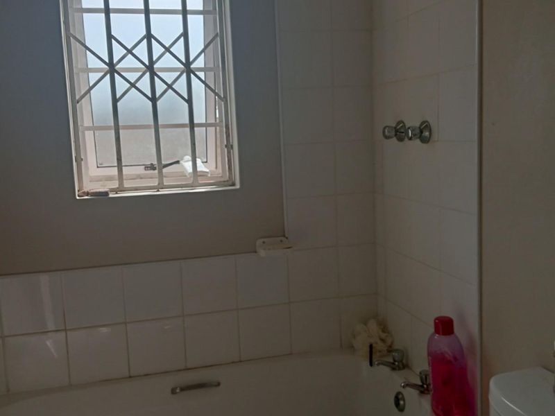 A functional bathroom featuring a standard bathtub with tiled surround and a window fitted with security bars.
