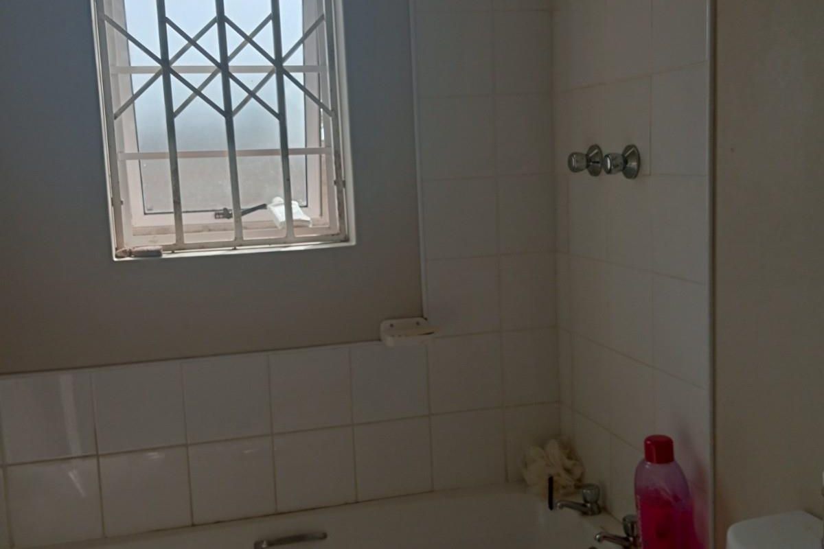 A functional bathroom featuring a standard bathtub with tiled surround and a window fitted with security bars.