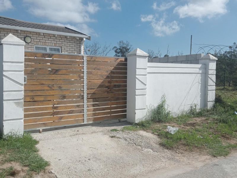 Front exterior view featuring a wooden sliding gate, perimeter wall, and concrete driveway access to the brick-faced house.