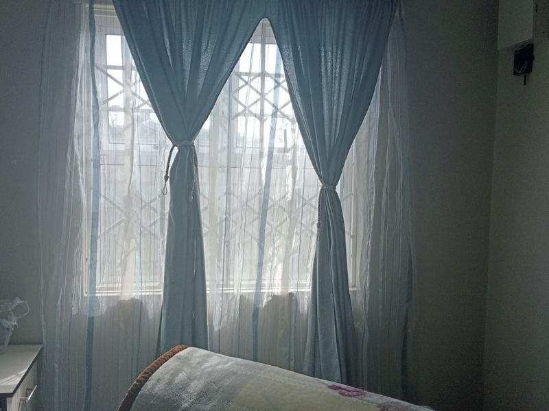 A bedroom featuring a window with a fitted security gate and curtains.