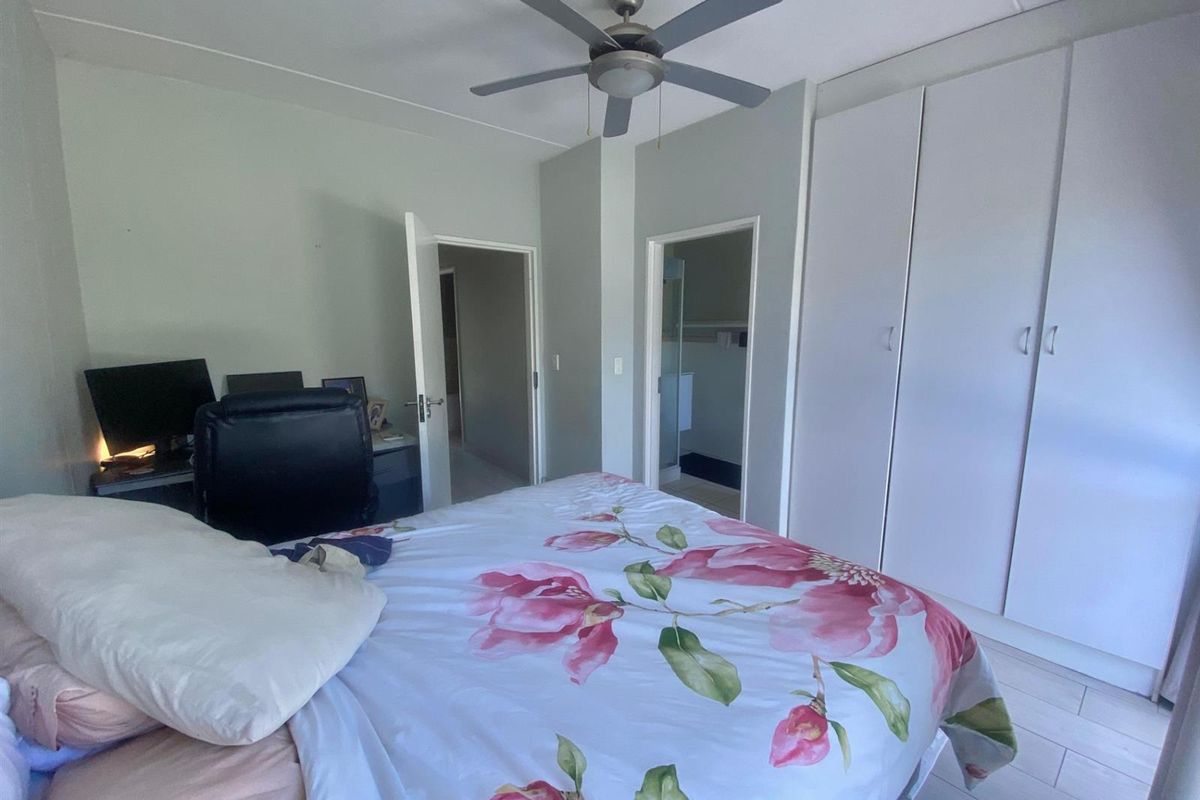 A bedroom featuring built-in cupboards, a ceiling fan, and tiled flooring, with an adjoining en-suite bathroom.
